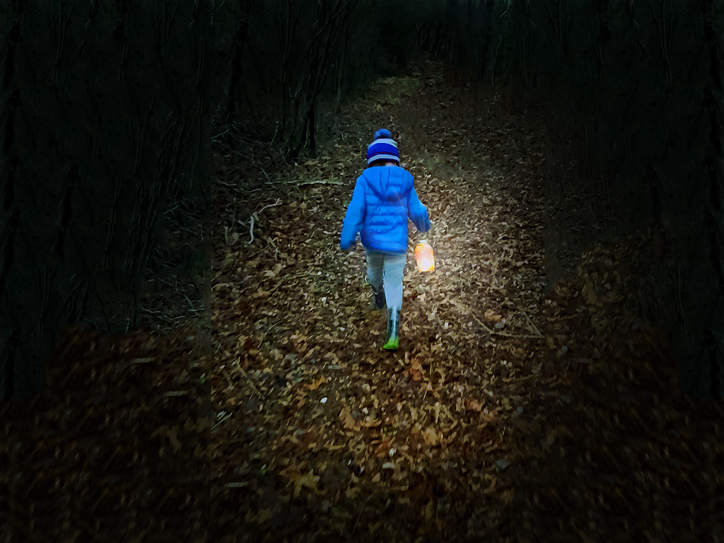 Young boy walking on a path in the woods at nighttime carrying a homemade mason jar lantern.