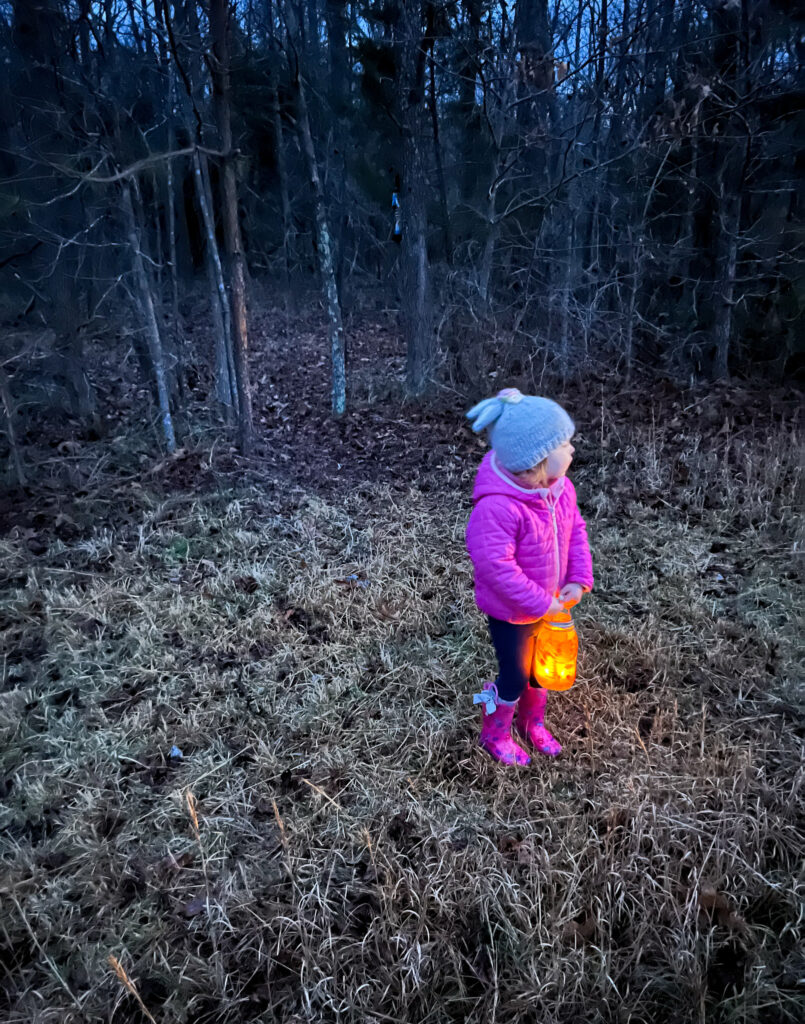 Young girl outside at night carrying homemade mason jar lantern.