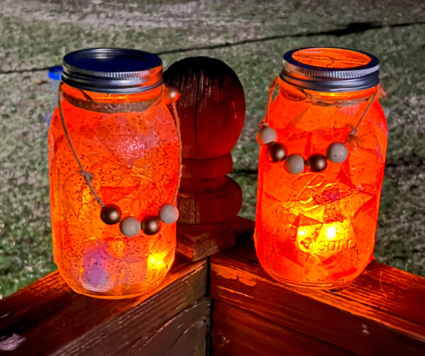 Two Mason jars decorated with a colorful assortment of tissue paper. Jars are lite at night.