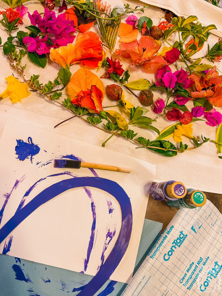 Display of flowers, paint, paint brush, cardboard, and transparent paper.