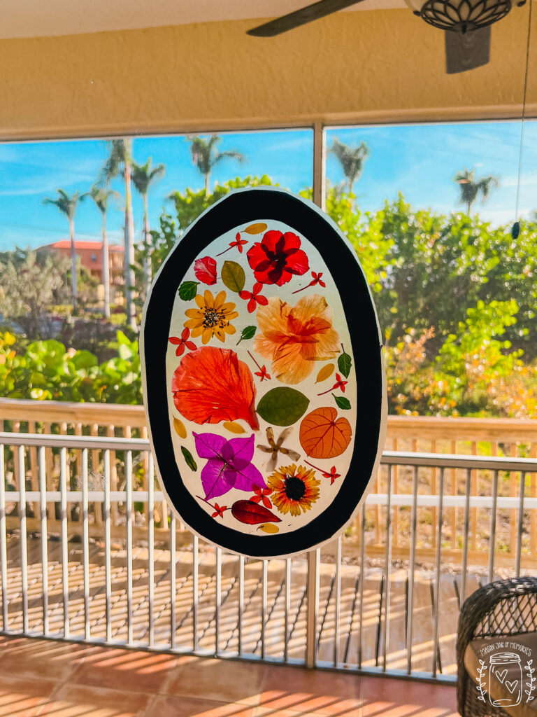 Beautiful flower suncatcher displayed on outdoor window in front of palm tree.