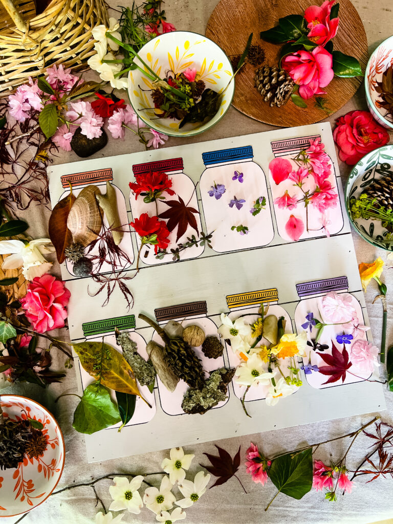 Table full of beautiful nature items from children's scavenger hunt, such as flowers, sticks, grass, rocks, shells, and weeds.