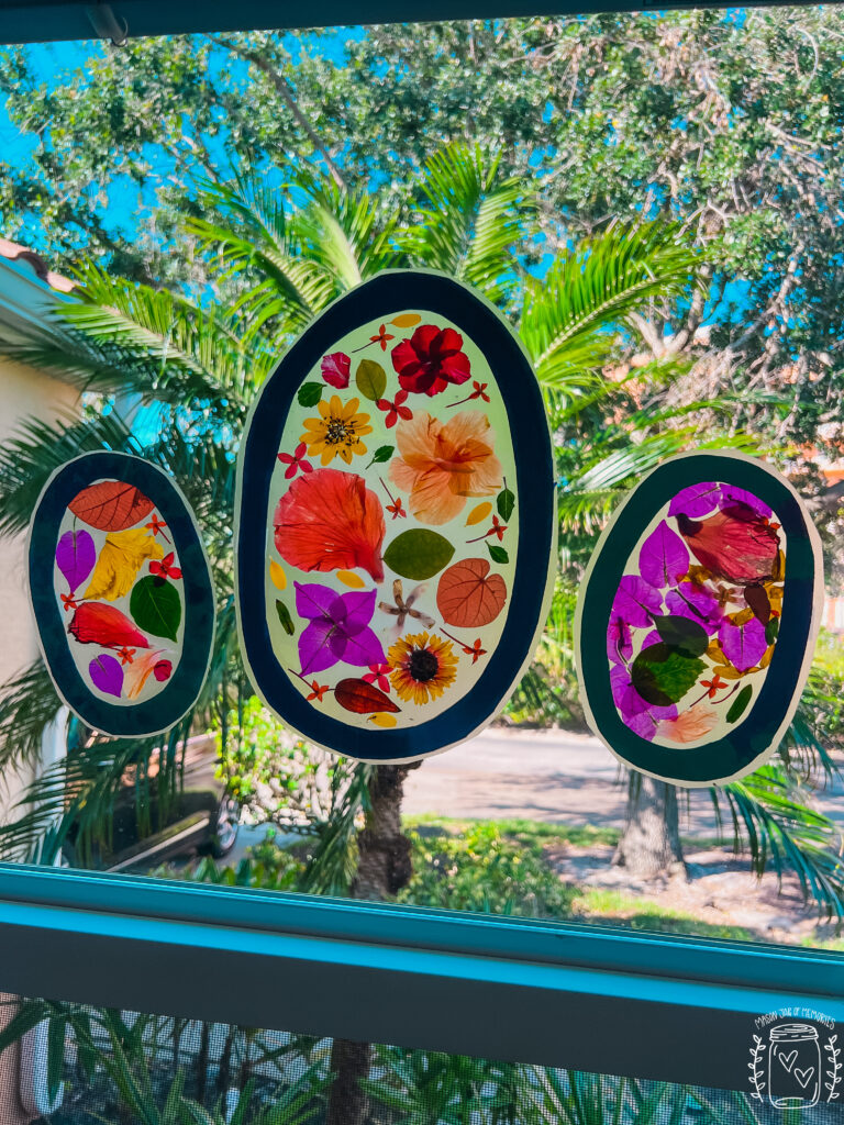 Three oval-shaped flower suncatchers displayed on a window with a palm tree in the background.