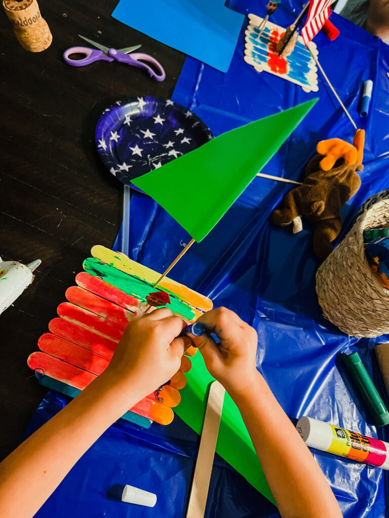 DIY Boat made out of popsicle sticks with toddlers hands working.