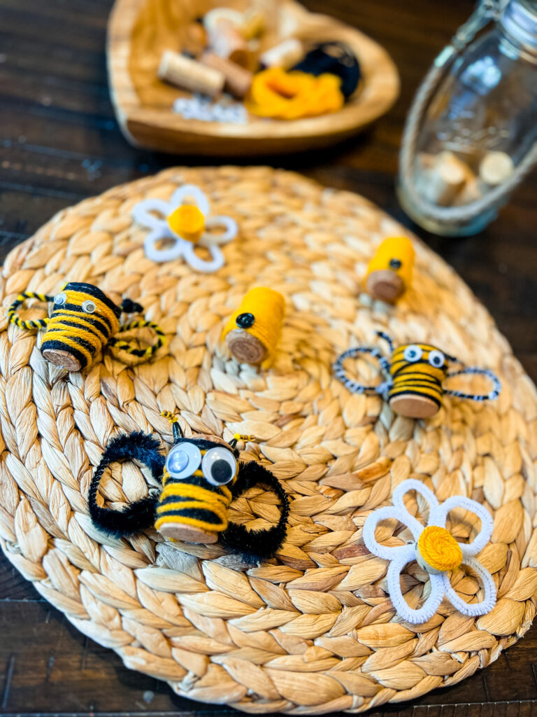 Honeybee theme craft consisting of honeybees, hives, and flowers made from yarn, googly eyes, pipe cleaners, and wine corks.