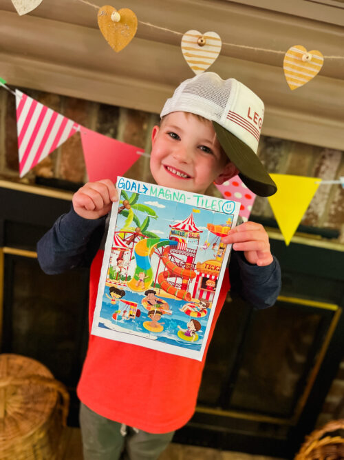 Toddler boy holding up completed sticker puzzle for showing strong work ethic.