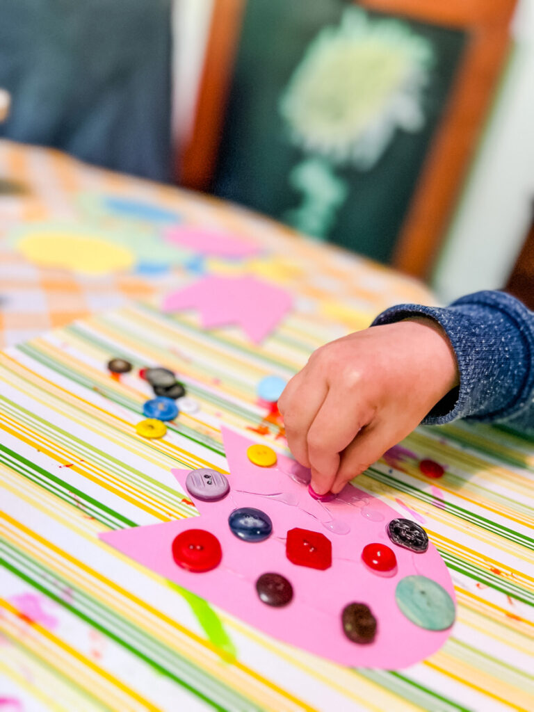 Preschool boy's hand placing buttons on his spring flower craft.