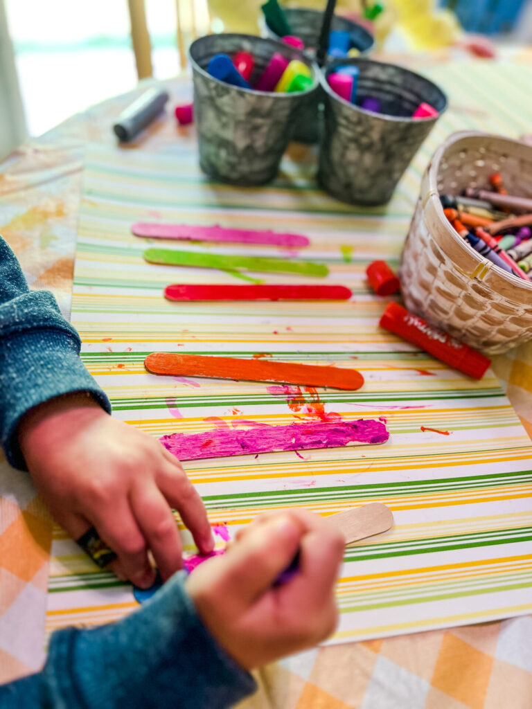 Preschool Child's hand using paint sticks to color popsicle stick flower stem.
