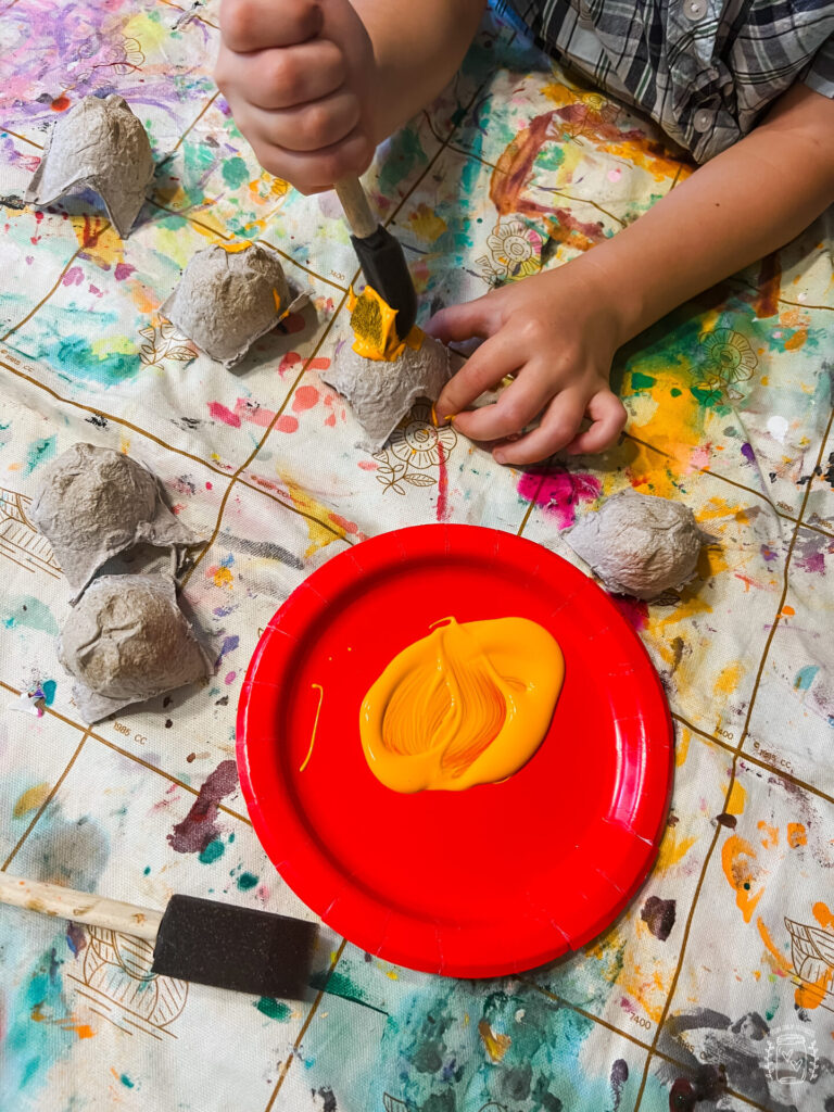 Egg Carton Pumpkins, young boy painting the egg carton sections with orange paint.