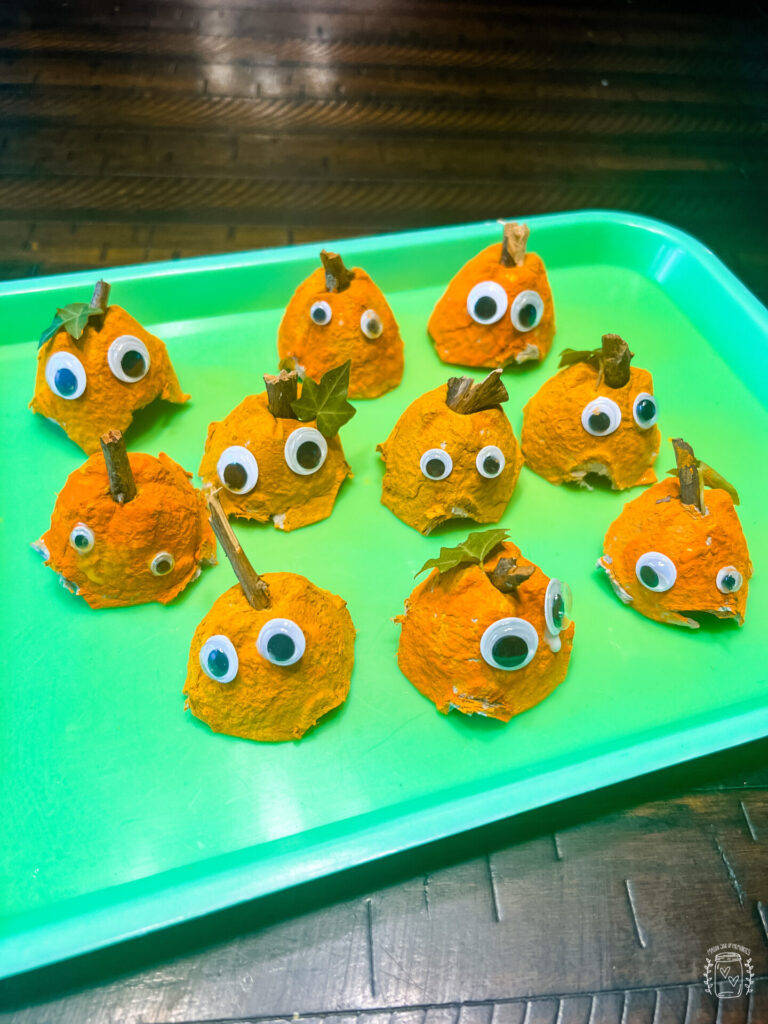 Egg Carton Pumpkins with googly eyes on a green tray.