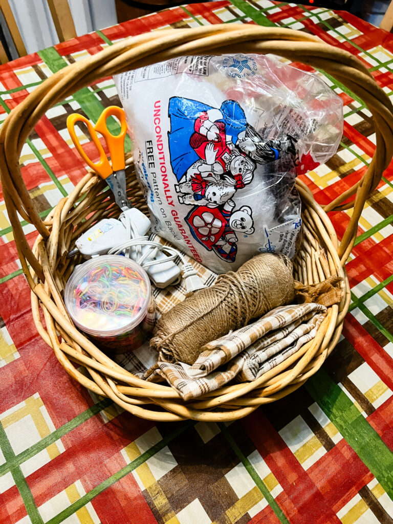 Fabric Pumpkins materials in a basket. Materials include stuffing, fabric, burlap, twine, hot glue gun, scissors. 