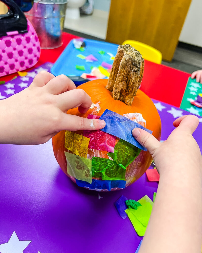 Pumpkin Craft, Child's hand placing squares of tissue paper on the Mod Podge on the pumpkin.