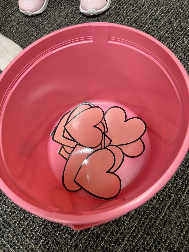 Color Matching Game for Valentine's Day for Toddlers and Preschoolers. Picture of a pink bucket with pink paper hearts inseide.
